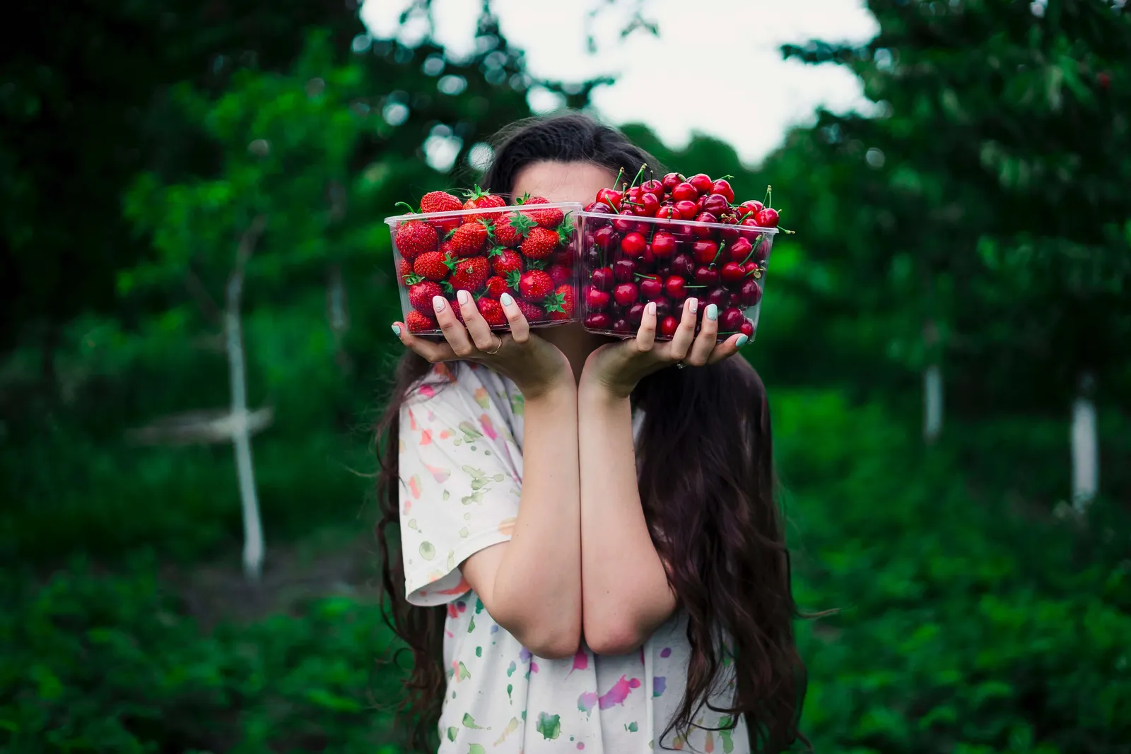 Mujer con el rostro cubierto por una canasta de fresas, en un entorno verde