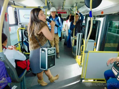 Mujer con chaleco de leopardo cantando con un parlante portátil dentro de un bus articulado