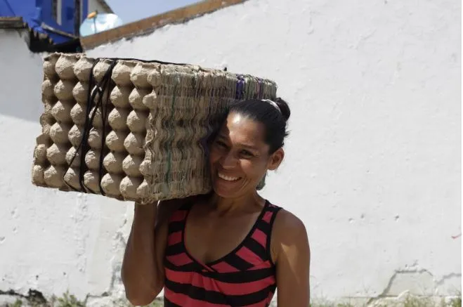 Mujer sonriente cargando sobre el hombro un gran cartón de huevos