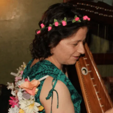 Mujer con corona de flores y vestido verde toca un instrumento de cuerda de madera