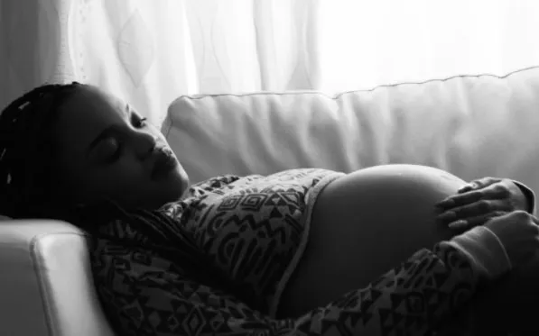 Mujer embarazada recostada en un sofá con las manos sobre el vientre, en blanco y negro