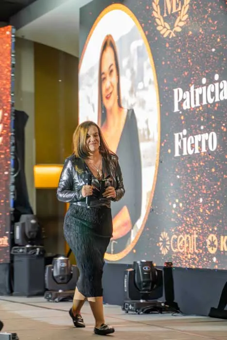 Mujer caminando por el escenario junto a una pantalla que muestra el nombre «Patricia Fierro» en la gala Mujeres Épicas