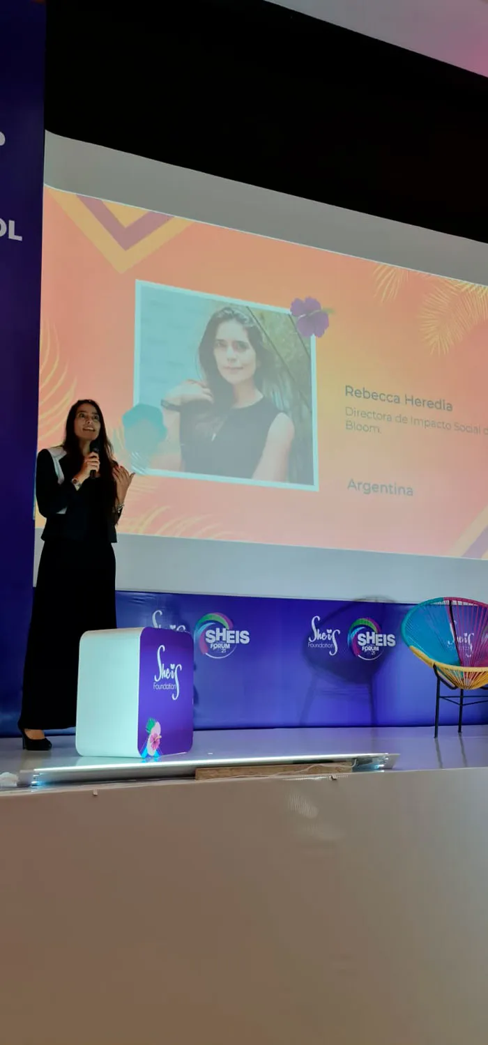 Mujer de pie en el escenario del foro con el retrato de una oradora proyectado en la pantalla