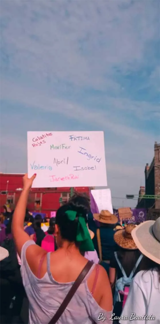 Mujer de espaldas levanta un cartel con nombres escritos a mano en la marcha del 8M