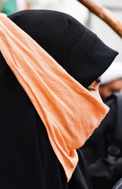 Perfil de una mujer con hiyab negro y un velo naranja sobre el rostro