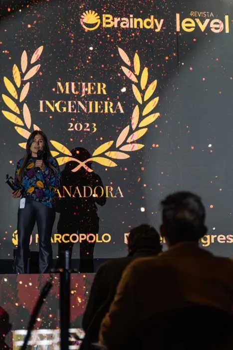 Mujer en el escenario frente a la pantalla «Mujer Ingeniera 2023, Ganadora» con los logos de Braindy y Revista Level