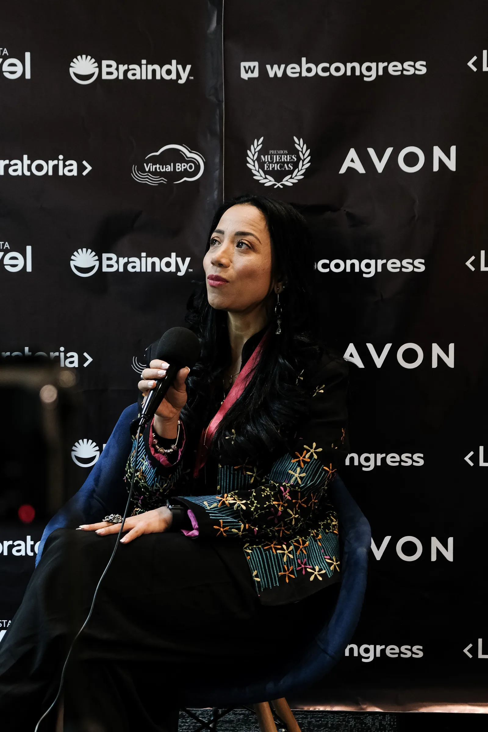 Mujer con micrófono sentada ante un panel de patrocinadores en los Premios Mujeres Épicas de Revista Level