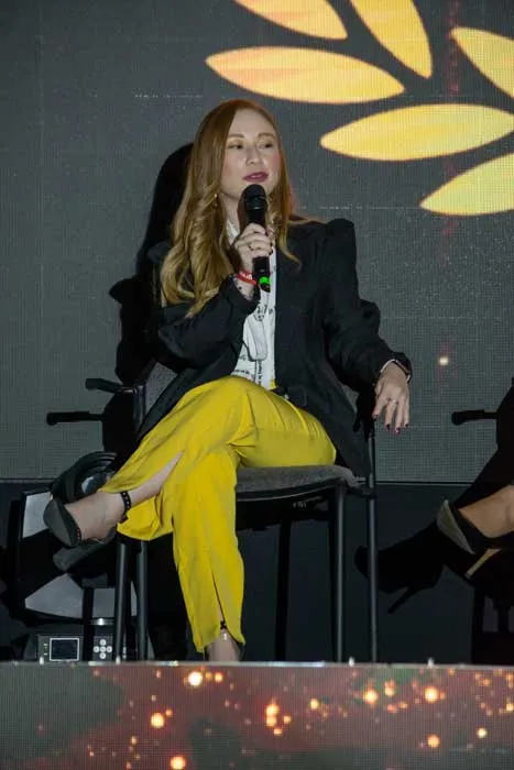 Mujer sentada con micrófono en la mano y pantalón amarillo durante un panel de los Premios Mujeres Épicas