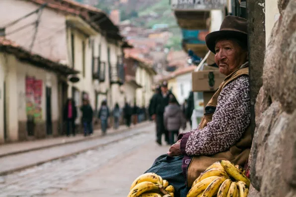 Mujer con sombrero sentada en una calle empedrada junto a un racimo de plátanos