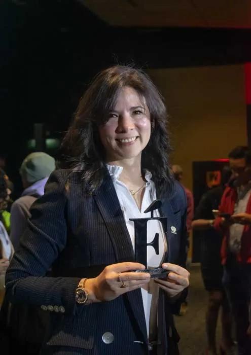 Mujer sonriente de blazer oscuro sostiene un trofeo en la gala de los Premios Mujeres Épicas