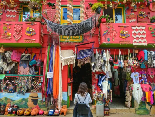 Mujer de espaldas frente a una tienda de artesanías de fachada roja muy colorida, con mochilas y textiles