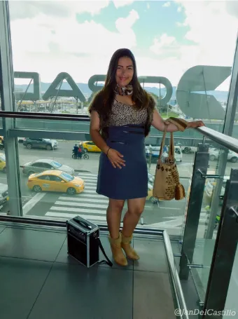 Mujer con vestido azul y bolso posando junto a un parlante portátil en un mirador de vidrio