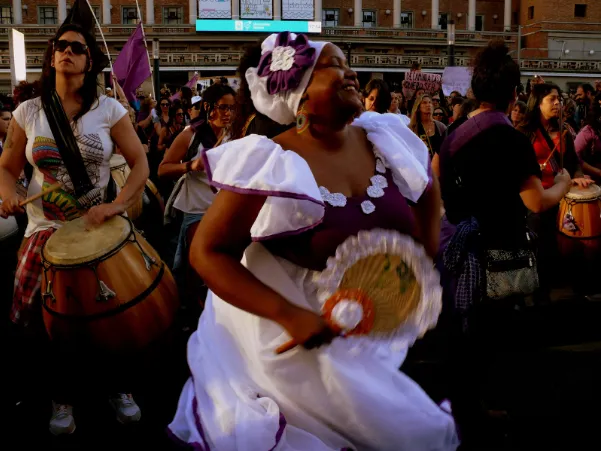 Mujer con vestido blanco y morado bailando junto a tamborileros en una marcha feminista
