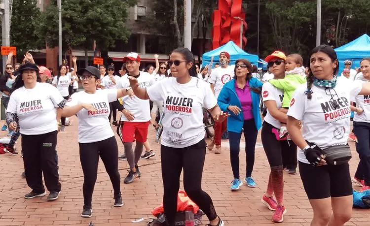 Grupo de mujeres con camisetas blancas «Mujer poderosa» baila en una plaza durante la ciclovía