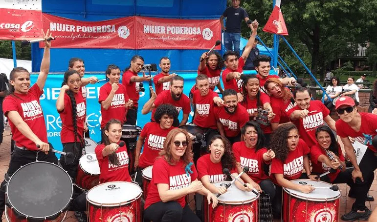 Grupo de mujeres con camisetas rojas «Mujer poderosa» tocan bombos en la ciclovía