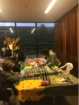 Mujeres cosiendo y bordando telas de colores sobre una mesa larga, en un taller