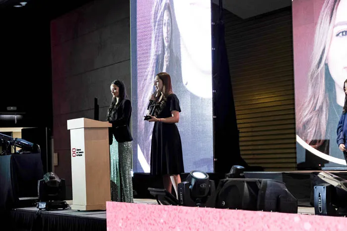 Dos mujeres en el escenario junto a un atril, con una pantalla grande detrás, en la premiación Mujeres Épicas 2022