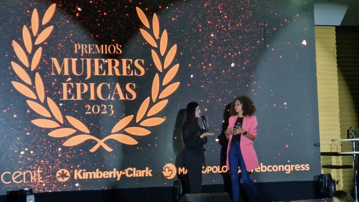 Dos mujeres conversan en el escenario ante el logo de los Premios Mujeres Épicas 2023