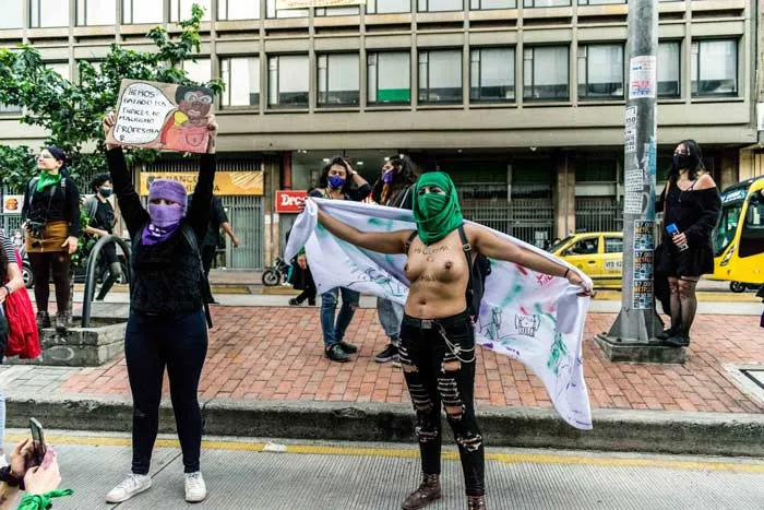 Dos mujeres con pañuelos morado y verde levantan carteles y una pancarta en una plaza durante la marcha