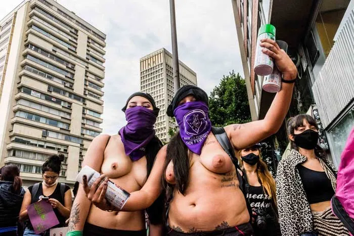 Mujeres con pañuelos morados en el rostro y el torso desnudo levantan el brazo con botellas en la marcha del 8 de marzo