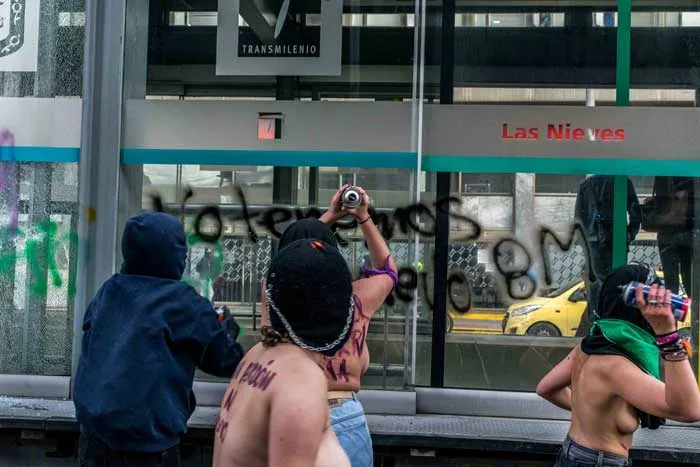 Mujeres con pañuelos en el rostro pintan grafitis sobre el vidrio de una estación de bus durante la marcha del 8 de marzo