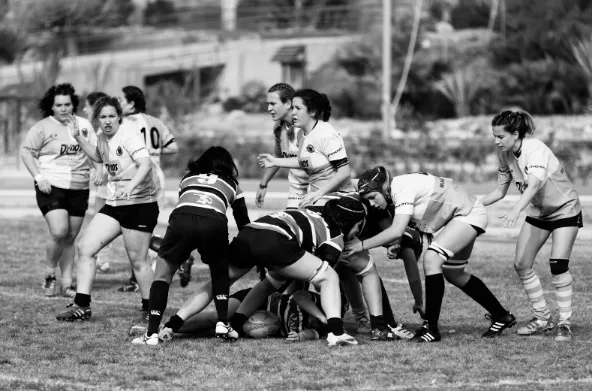 Equipo de mujeres juega rugby en un scrum sobre el campo, en blanco y negro