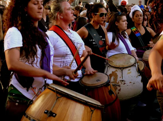 Mujeres tocando tambores en una marcha feminista, con fulares morados