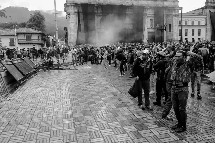 Multitud avanza por una plaza empedrada entre humo frente a un edificio durante la protesta