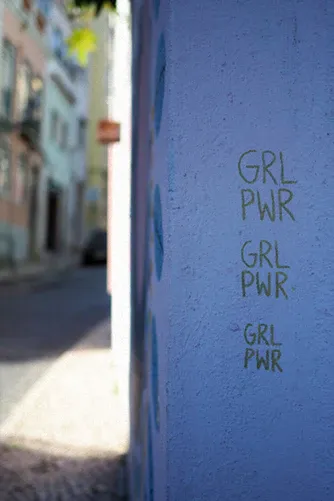 Muro azul en una calle estrecha con la frase «GRL PWR» escrita tres veces