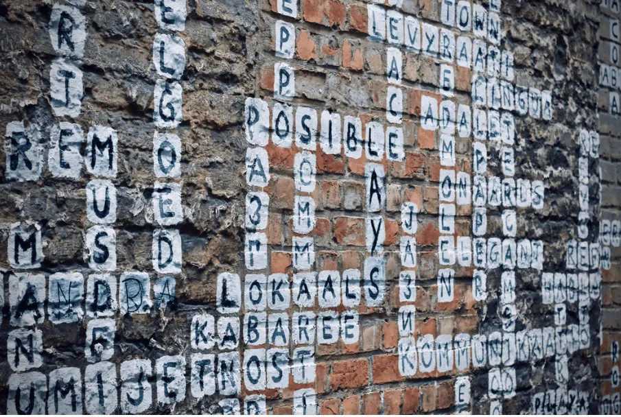 Muro de ladrillo con letras blancas pintadas que forman un crucigrama de palabras como «posible»
