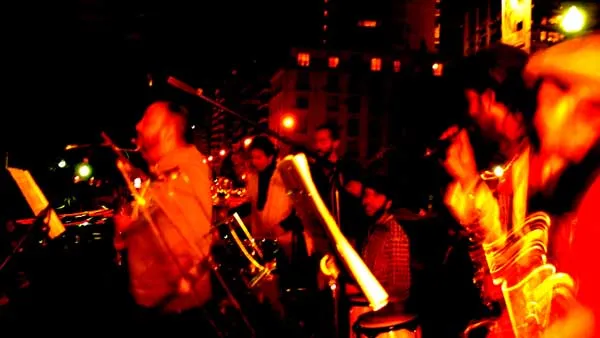 Músicos tocando instrumentos de viento en un ambiente nocturno de luces rojas