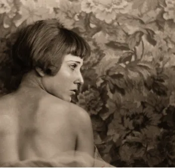 Retrato antiguo en sepia de Nahui Olin, de espaldas y con el rostro girado, ante un fondo de hojas