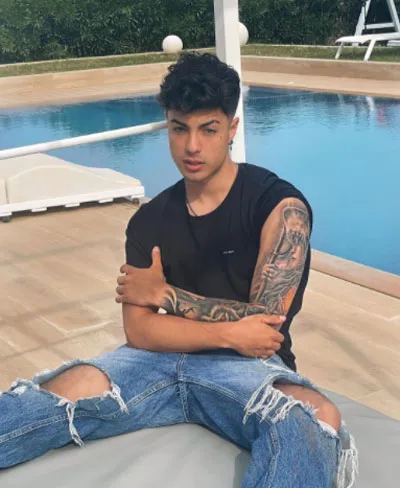 Naim Darrechi, joven de cabello oscuro y tatuajes en el brazo, sentado con los brazos cruzados junto a una piscina