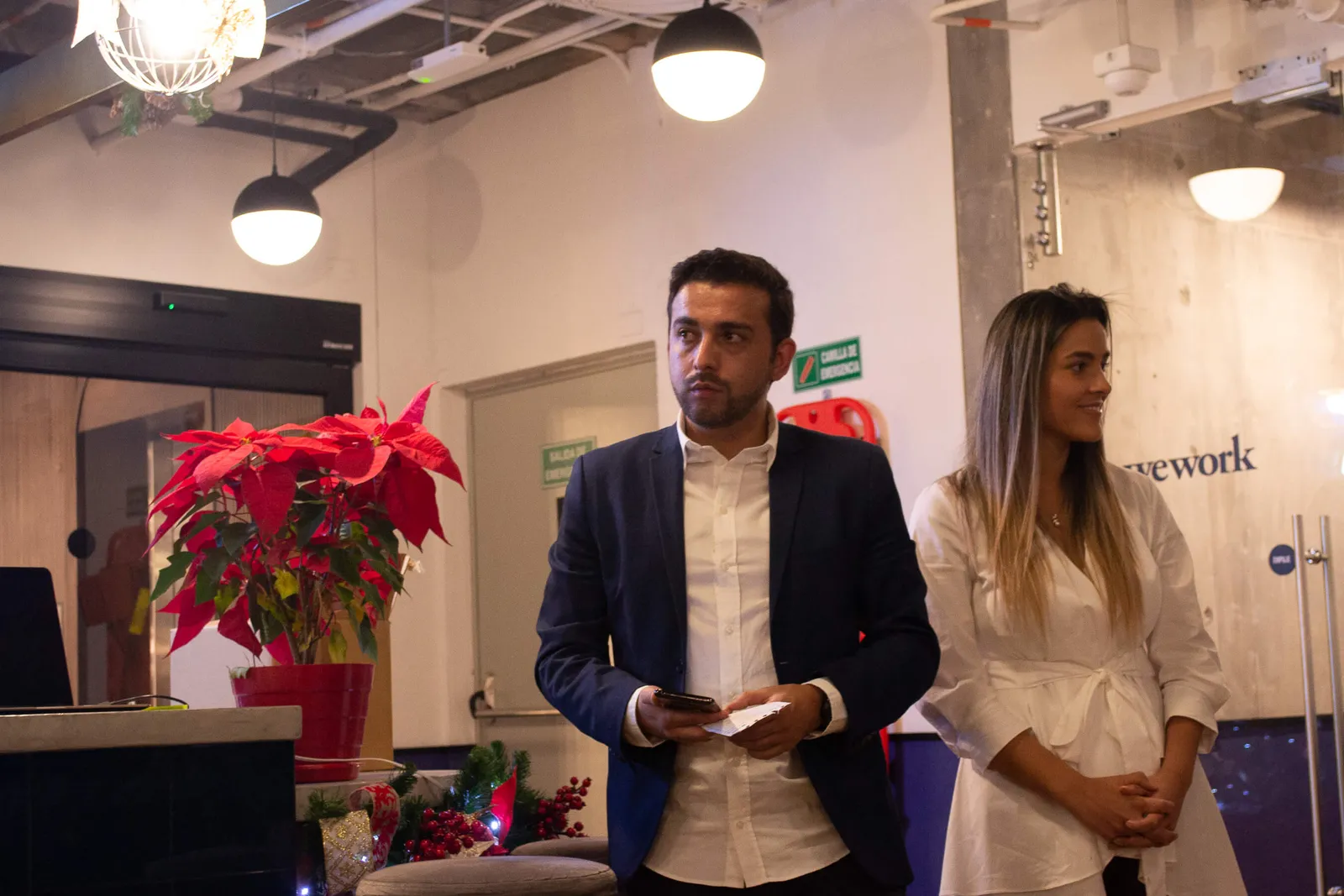Nicolás Márquez y Karol Franco, del equipo de Revista Level, de pie junto a una poinsettia en el evento de lanzamiento