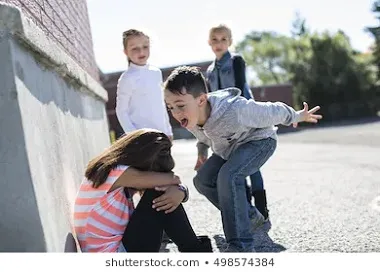 Niña sentada abrazando sus rodillas junto a un muro mientras un niño le grita con los brazos extendidos y otros dos observan