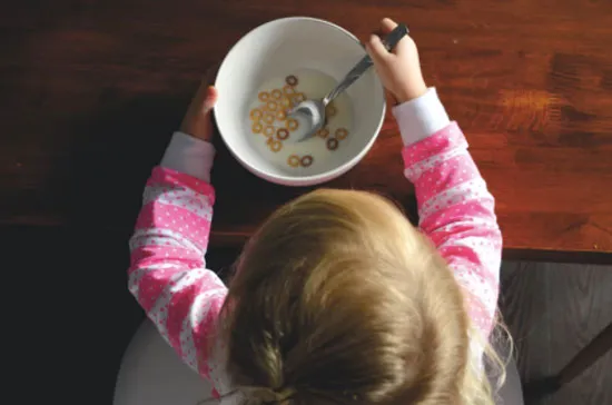 Niña vista desde arriba comiendo cereal con una cuchara en un tazón blanco