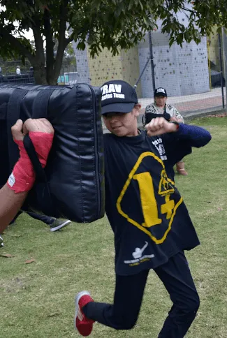 Niña con gorra y camiseta azul oscura carga un escudo de golpeo durante un entrenamiento de krav magá