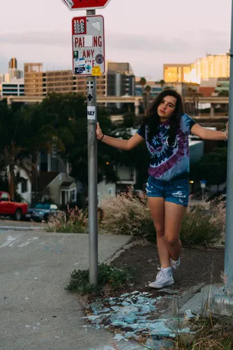 Niña con camiseta estampada apoyada en un poste de señal en una calle de ciudad