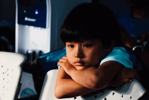 Niño con expresión seria apoya la cabeza sobre sus brazos cruzados frente a un equipo de laboratorio