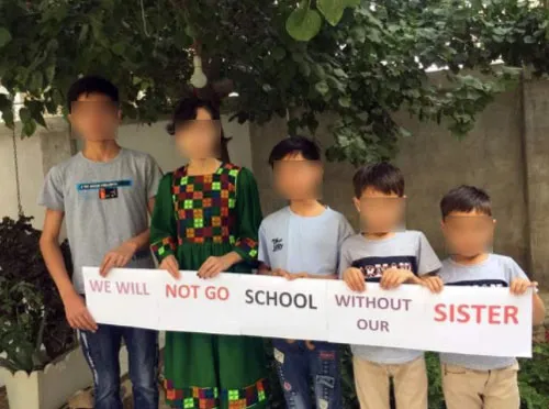 Niños con el rostro difuminado sostienen un cartel «We will not go school without our sister» junto a una niña con vestido tradicional