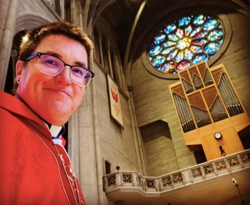 Obispo con camisa clerical roja y gafas se toma un selfi dentro de una iglesia con vitral y órgano
