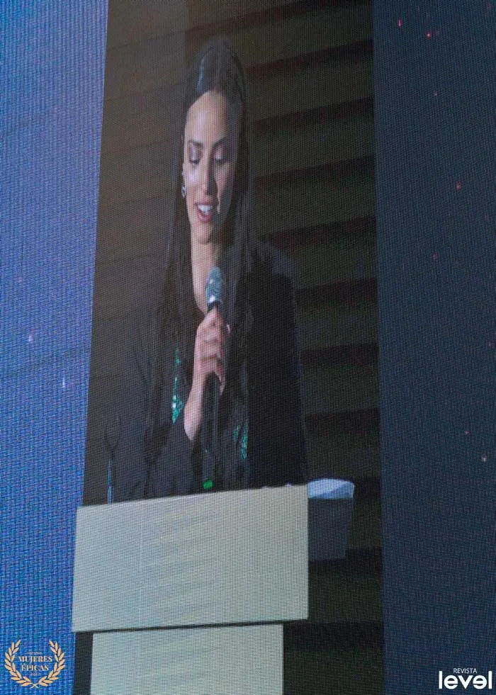 Oradora con micrófono proyectada en una pantalla grande durante los premios Mujeres Épicas de Revista Level