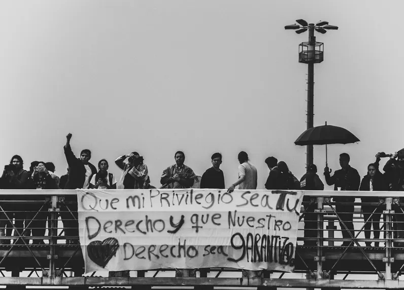 Manifestantes sobre un puente peatonal con una pancarta «Que mi privilegio sea tu derecho y que nuestro derecho sea garantizado»