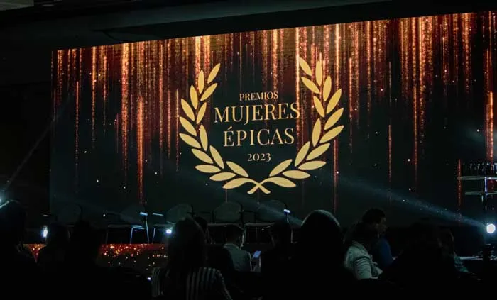 Pantalla del escenario con el logo de laurel «Premios Mujeres Épicas 2023» sobre un fondo de luces doradas