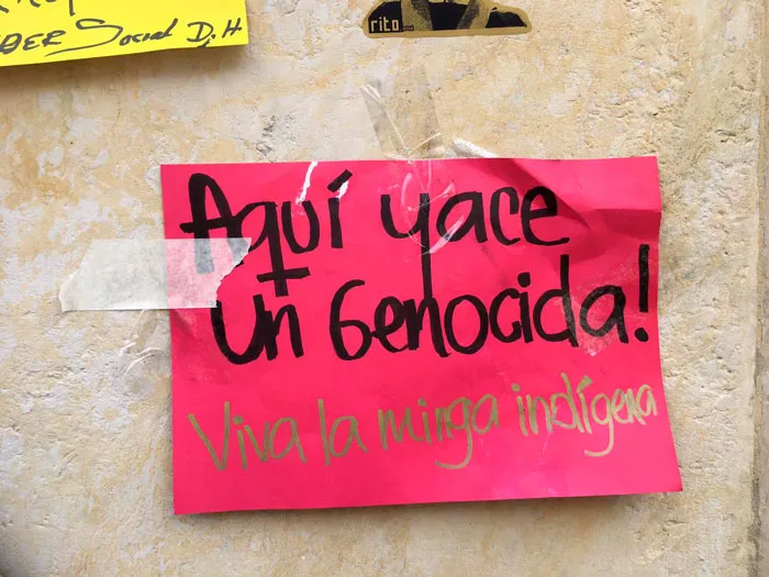 Papel rosado pegado en un muro con el mensaje «Aquí yace un genocida! Viva la minga indígena»