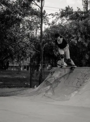 Patinadora con protecciones se lanza desde lo alto de una rampa de skatepark, en blanco y negro