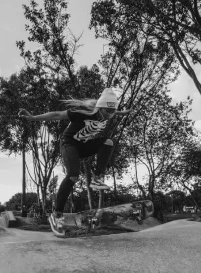 Patinadora en pleno salto con su tabla en un skatepark entre árboles, en blanco y negro