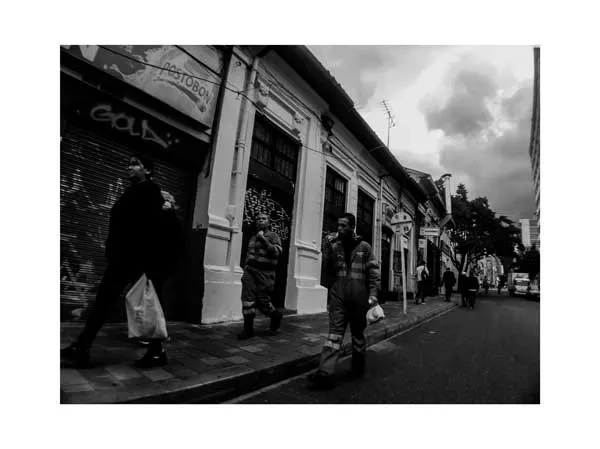 Peatones con tapabocas caminan por una calle del centro con fachadas antiguas, en blanco y negro