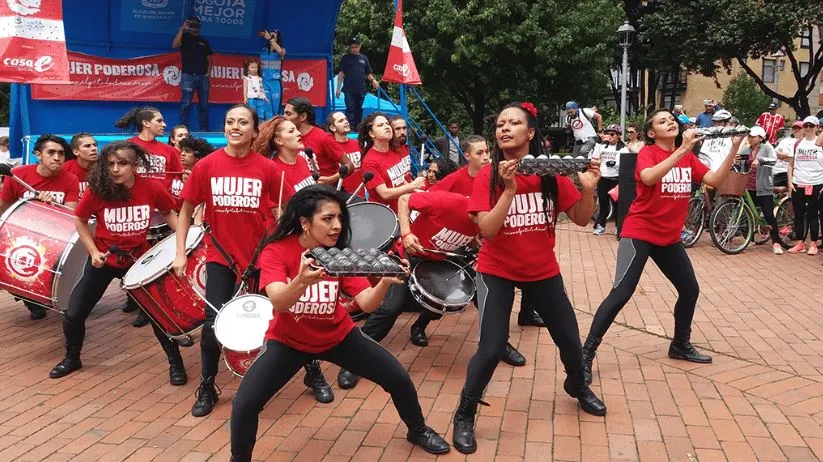 Grupo de percusionistas con camisetas rojas toca tambores y baila sobre el pavimento de una plaza