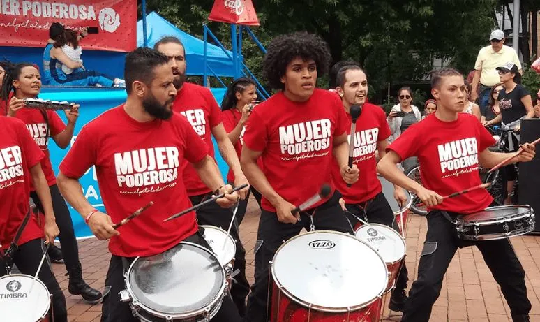 Percusionistas con camisetas rojas «Mujer poderosa» tocan tambores en una plaza